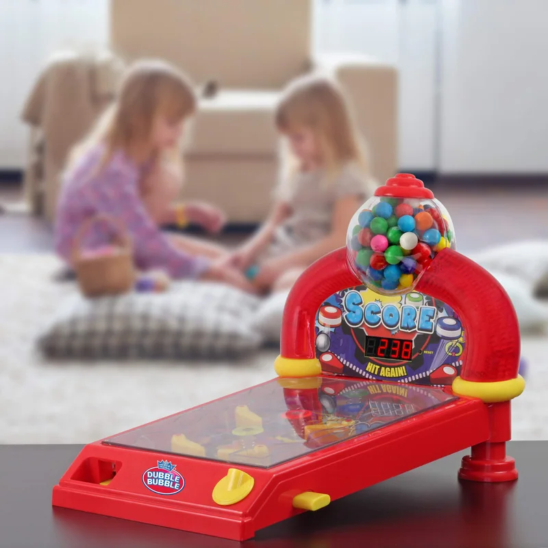 A Dubble Bubble pinball gumball machine on a table, two children playing on the rug behind it